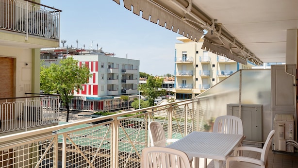 A balcony with a table and chairs, a view of the street, and a building with balconies. - Apartment 'San Paolo 07' with Private Terrace and Air Conditioning (Lido di Jesolo)