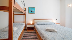 A room with bunk beds, a bedside table with a lamp, a wall-mounted artwork, and a striped rug. - Apartment 'San Paolo 07' with Private Terrace and Air Conditioning (Lido di Jesolo)