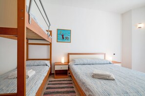 Una stanza con letti a castello, un comodino con una lampada, un’opera d’arte appesa al muro e un tappeto a righe.