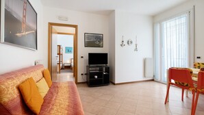 A living room with a sofa, TV stand, and dining area. - Apartment 'San Paolo 07' with Private Terrace and Air Conditioning (Lido di Jesolo)