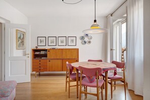 Un coin repas avec un buffet en bois, une table recouverte d’une nappe à motifs et des chaises roses.