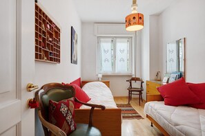 Une chambre à coucher comprenant un lit, une chaise, une commode, une fenêtre avec des rideaux et une étagère fixée au mur.