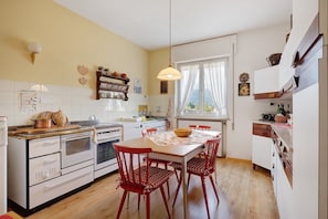 Une cuisine avec des meubles blancs, une table en bois, des chaises rouges et un luminaire suspendu.