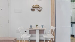 Una cocina moderna con armarios blancos, un refrigerador blanco y un comedor con mesa y sillas blancas.