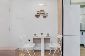 Una cocina moderna con armarios blancos, un refrigerador blanco y un comedor con mesa y sillas blancas.