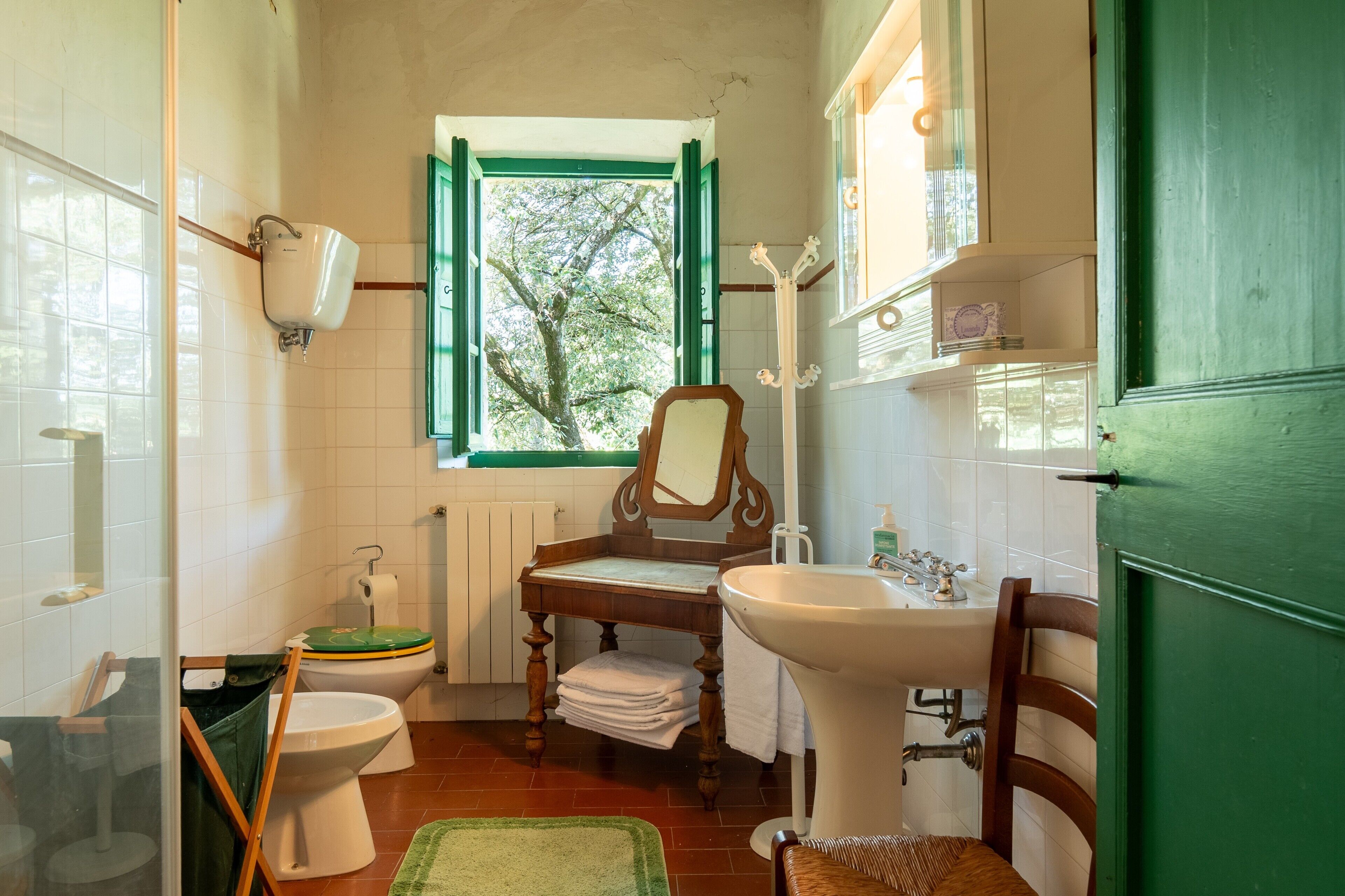 Un bagno con il water, lavandino, specchio e finestra vista alberi.