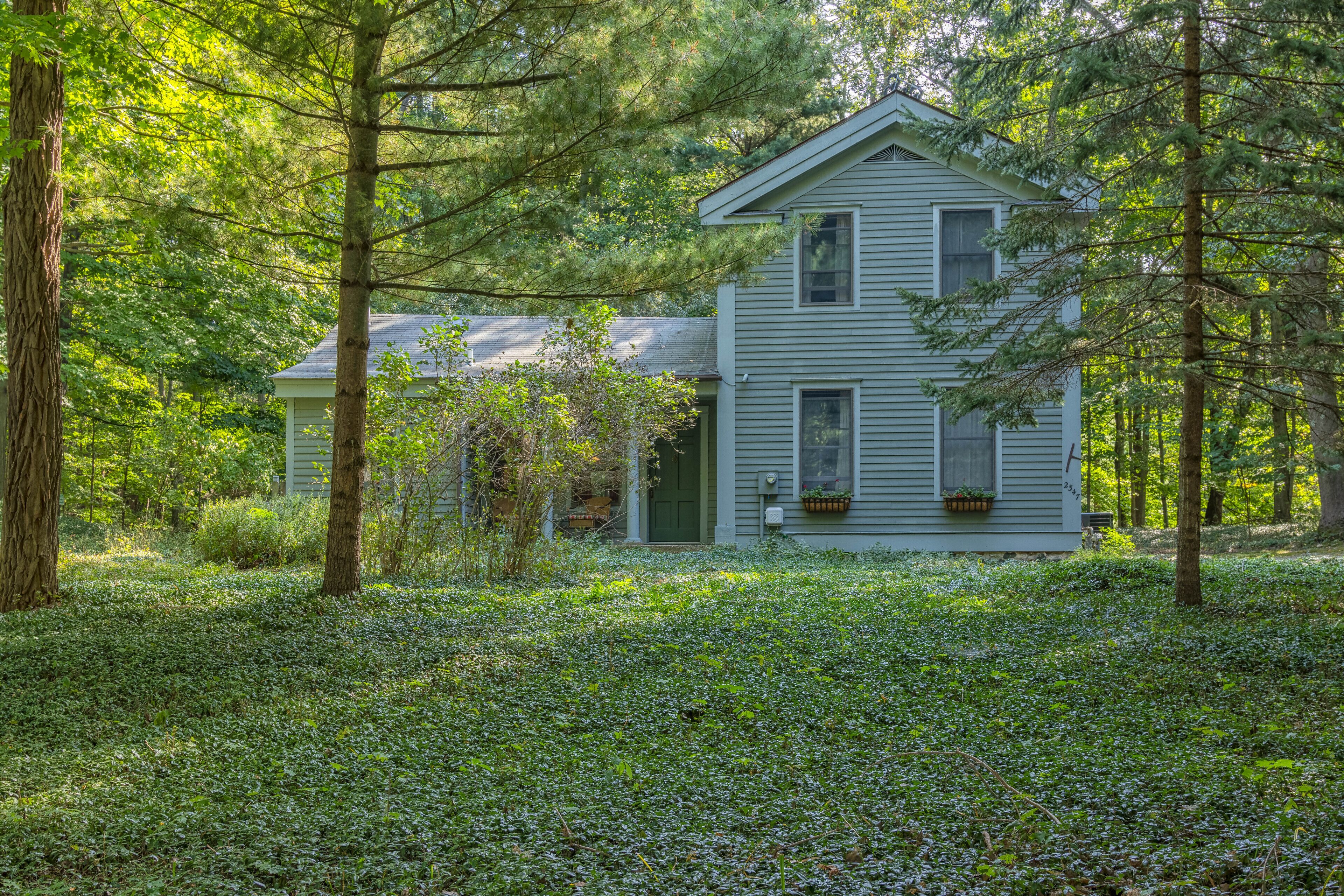 Une maison à deux étages entourée d’une forêt dense.