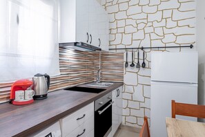 A kitchen with a stone-patterned backsplash, a stainless steel kettle, a red coffee maker, and a white refrigerator.