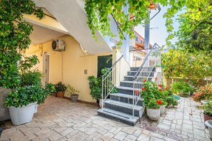 A stone-paved courtyard with a staircase, potted plants, and a building entrance.