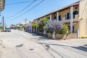 A street view with buildings, a parked car, and a flower box with purple flowers.