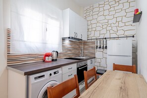 A compact kitchen with a washing machine, a coffee maker, and a refrigerator.