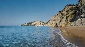 A beach with clear water, a sandy shore, and rocky cliffs.