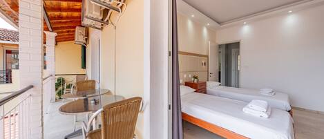 Quarto de hotel com varanda, uma cama, uma mesa com cadeiras e uma pequena cozinha.