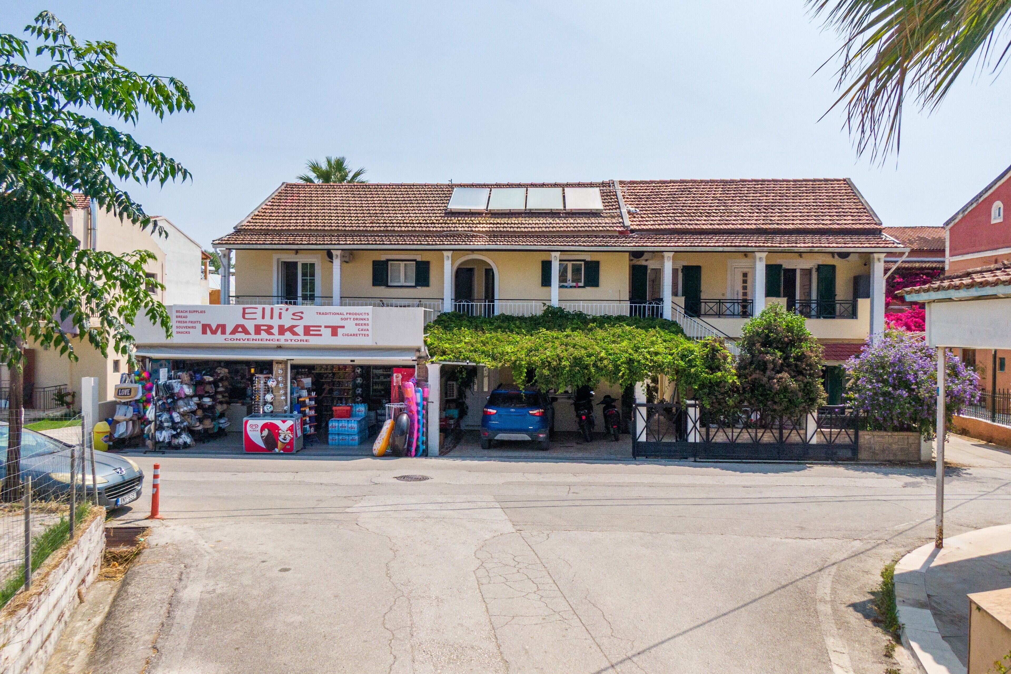Un bâtiment à deux étages, avec un toit recouvert de tuiles, une enseigne indiquant « Marché d’Elli » et une voiture garée devant.