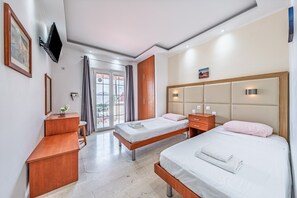 Ein Hotelzimmer mit zwei Betten, einem Holztisch, einem an der Wand montierten Fernseher und einem großen Fenster mit Vorhängen.