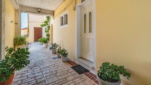 Un corridoio stretto con pavimento in pietra, piante in vaso, una porta bianca e una finestra.