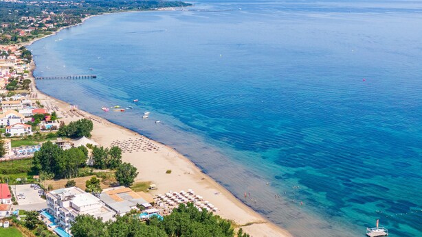 Vista aérea de una zona costera con playa, muelle y edificios a lo largo de la orilla.