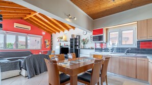 Una cocina moderna con armarios de madera, un comedor con mesa y sillas, y una pared roja con una ventana.