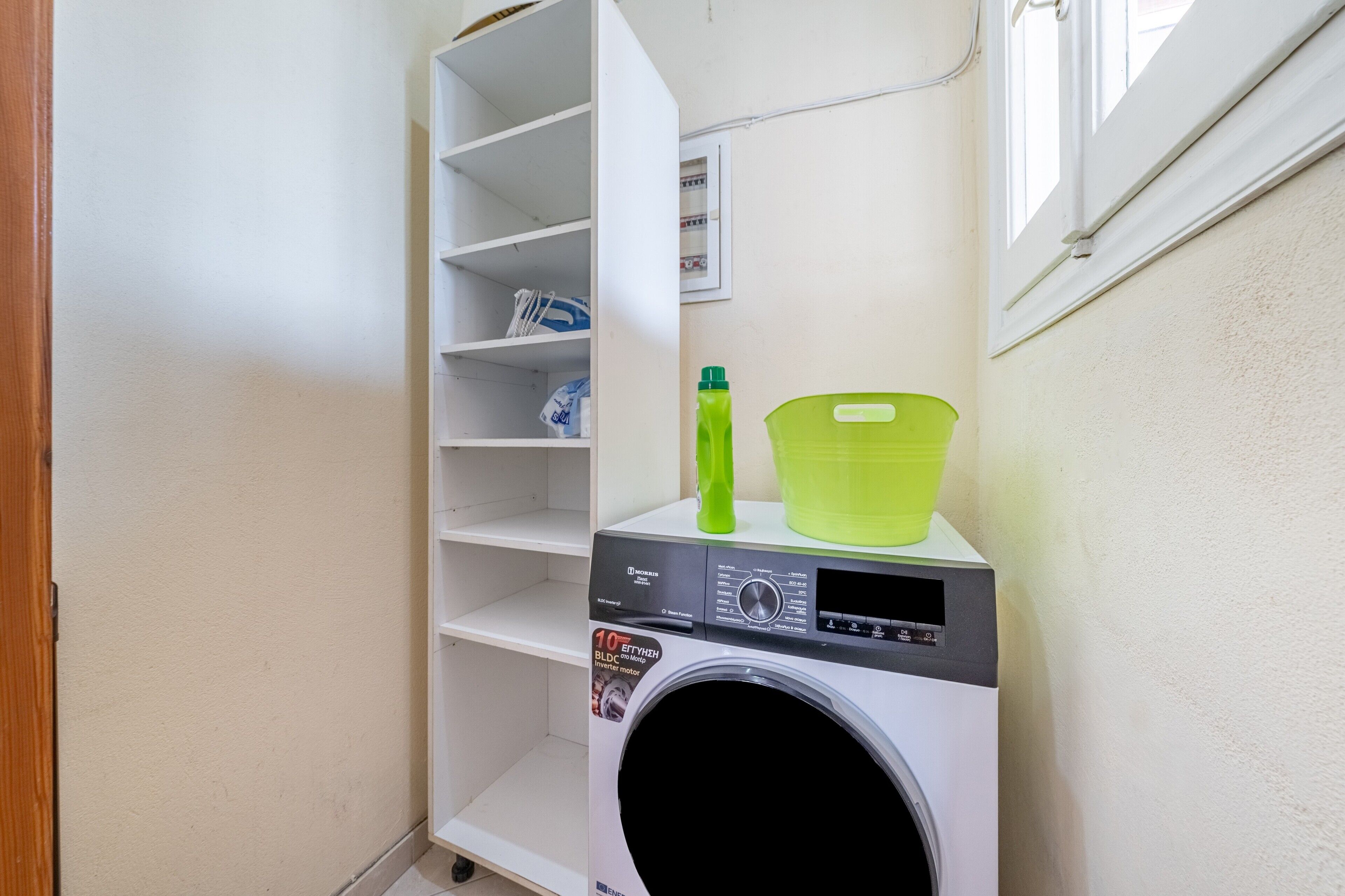 A laundry area with a washing machine, shelves, and a window.