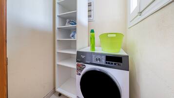 A laundry area with a washing machine, shelves, and a window.