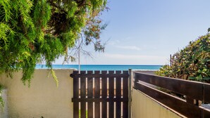 A gated entrance with a view of the sea, a white wall, and greenery.