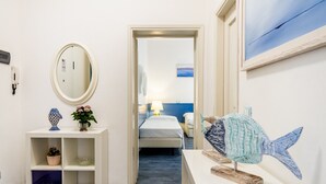 A hotel room with a bed, a bedside table with a lamp, a wall-mounted mirror, a shelf with decorative items, and a painting.