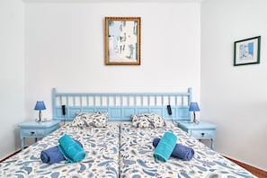 A double bed with patterned bedding, two bedside tables with lamps, a wall-mounted telephone, and two framed pictures. - Apartment 'Torresol 208' with Shared Pool, Wi-Fi and Air Conditioning (Nerja)