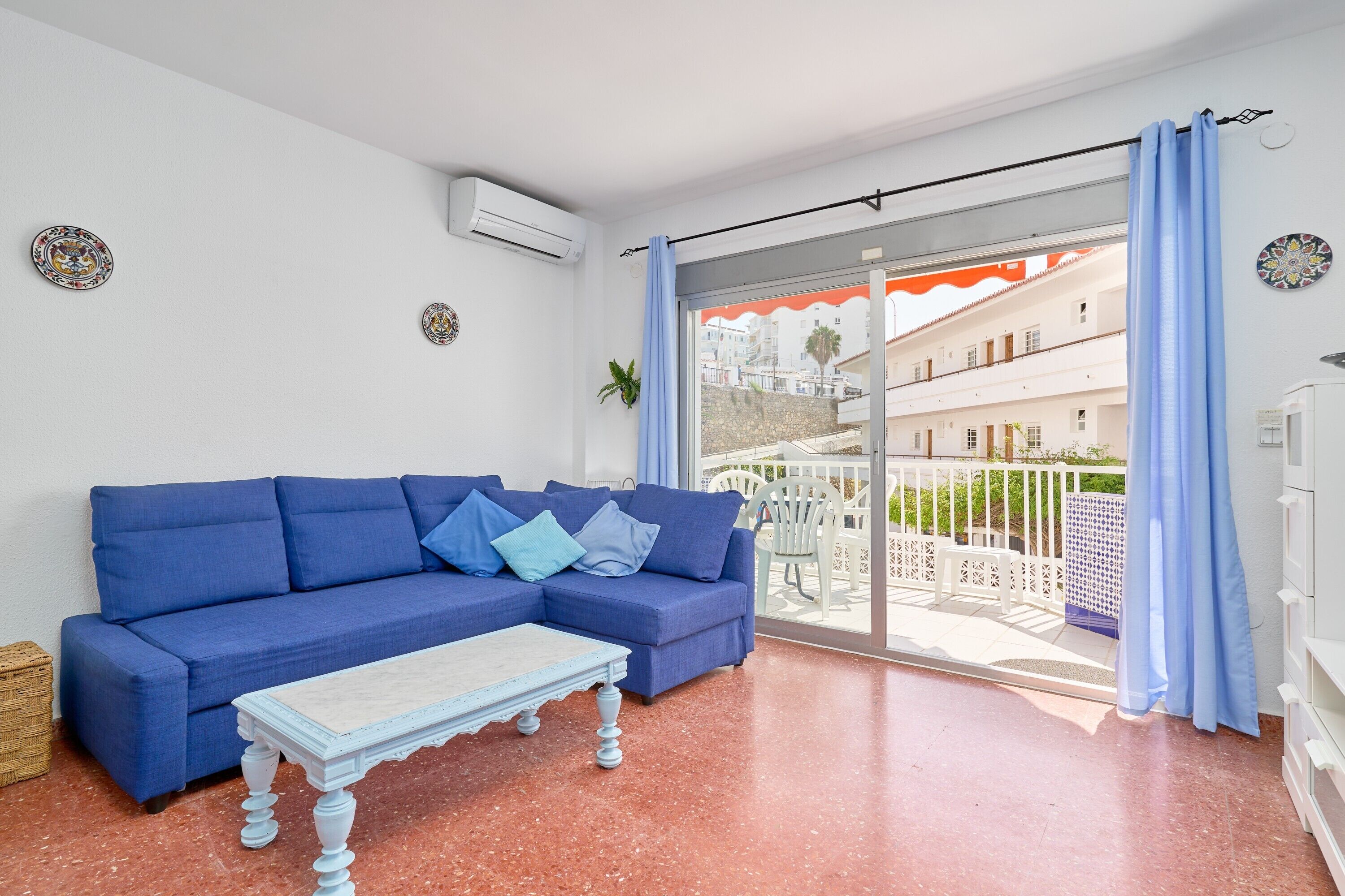 A blue sofa, a white coffee table, and a balcony with a view of buildings.
