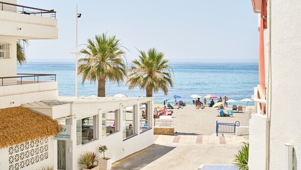 Een hotel aan de kust met een restaurant, terras, palmbomen en uitzicht op het strand.