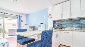 Een keuken met witte kastjes, een blauwe wand en een eetgedeelte met een tafel en stoelen.