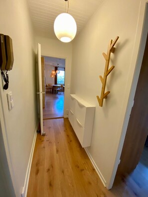 Ein Flur mit Holzboden, einer weißen Wand mit einer Holzdekoration und einer Pendelleuchte.