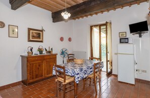 Un comedor con una mesa lista para cuatro, sillas de madera, un armario de madera, un ventilador y un refrigerador blanco.