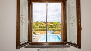 A room with a large window, a view of a swimming pool, and a wooden floor. - Apartment 'Casa Milla - Bilocale Becaccia' with Shared Pool, Shared Terrace and Wi-Fi (Cecina)
