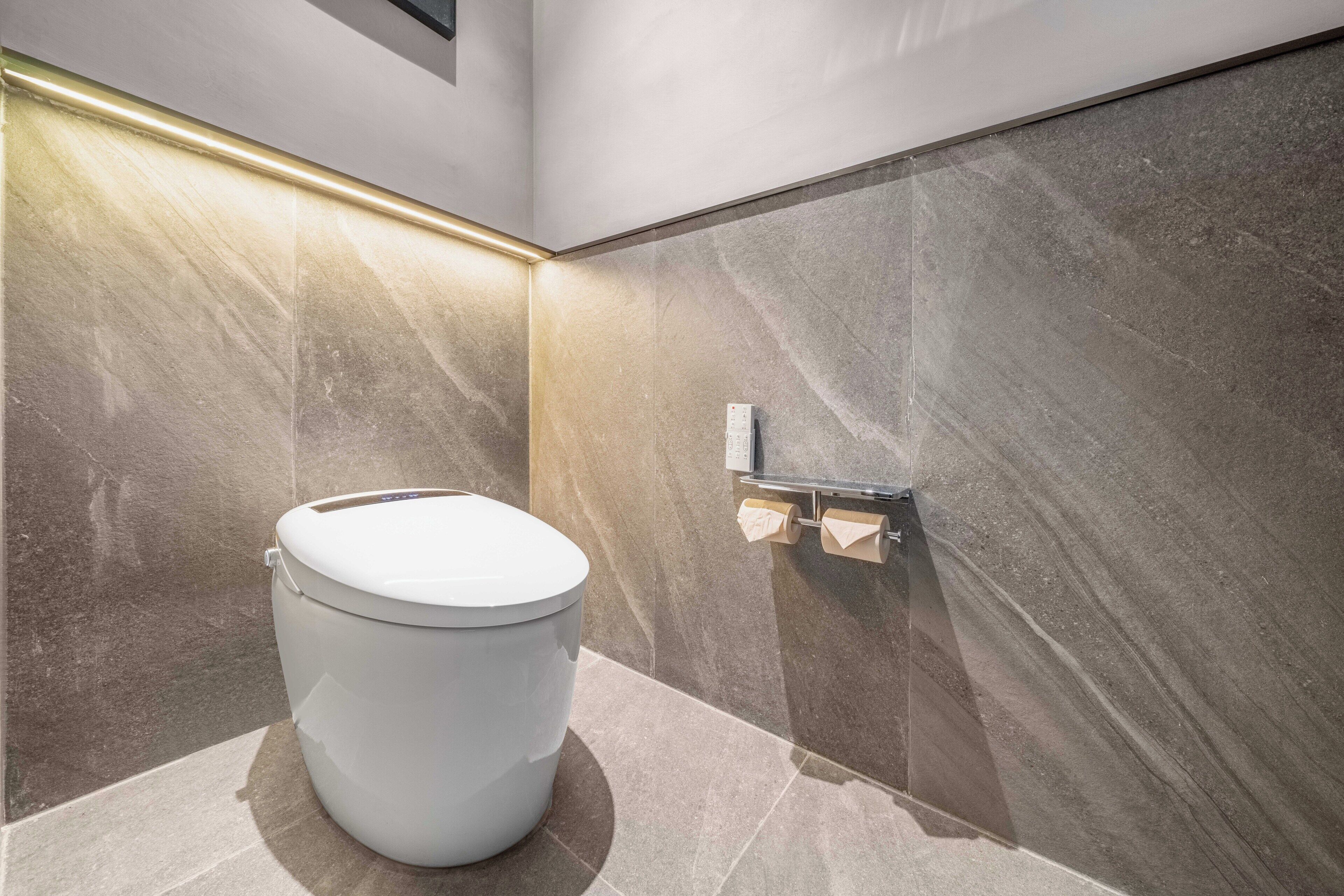 A modern bathroom with a white toilet, marble walls, and a towel dispenser.