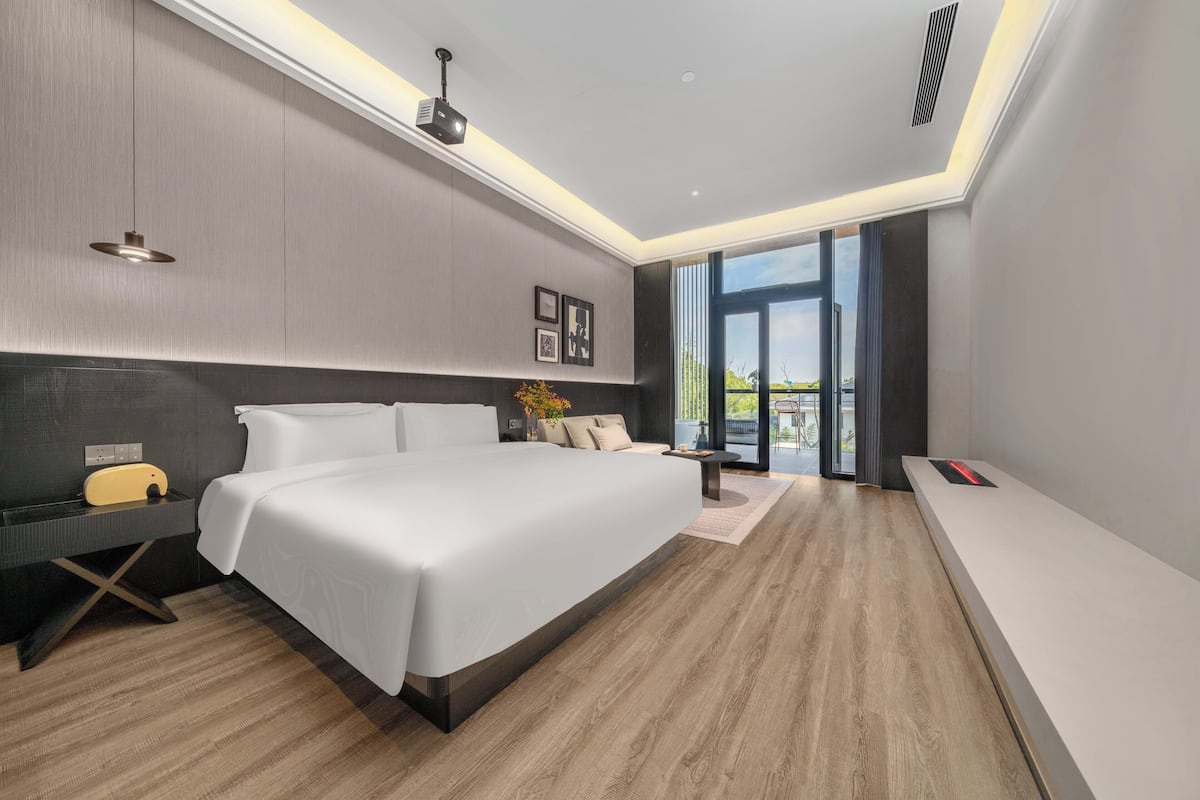 A modern hotel room with a large bed, a desk, and a view of the outdoors.