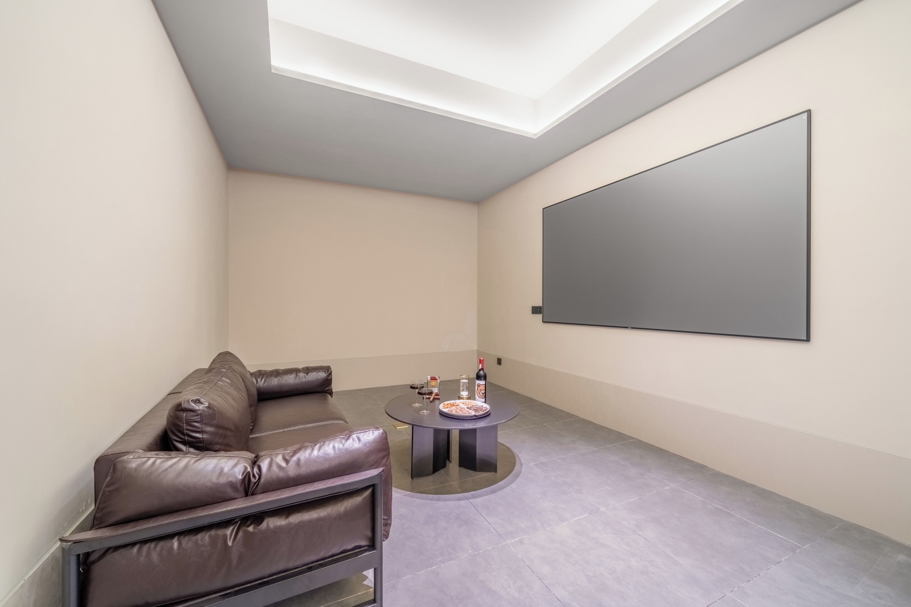 A modern living room with a brown leather sofa, a round coffee table, and a large flat-screen TV mounted on the wall.