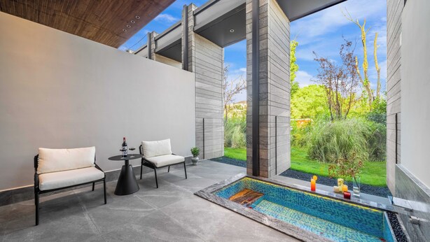 A modern outdoor seating area with a pool, two chairs, a table, and a view of a garden. - Songmo Hotel (Huzhou)
