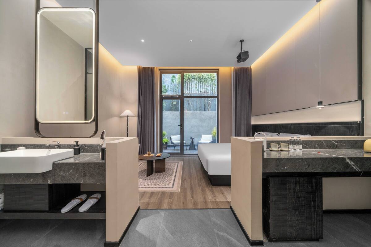 A modern hotel bathroom with two sinks, a large mirror, and a view of the outdoors.