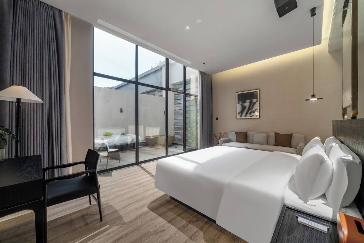 A modern hotel room with a large bed, a desk, and a view of the outside.