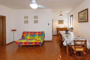 Een kamer met een kleurrijke bank, een eettafel met stoelen, een plafondventilator en lijstjes met foto's aan de muren.