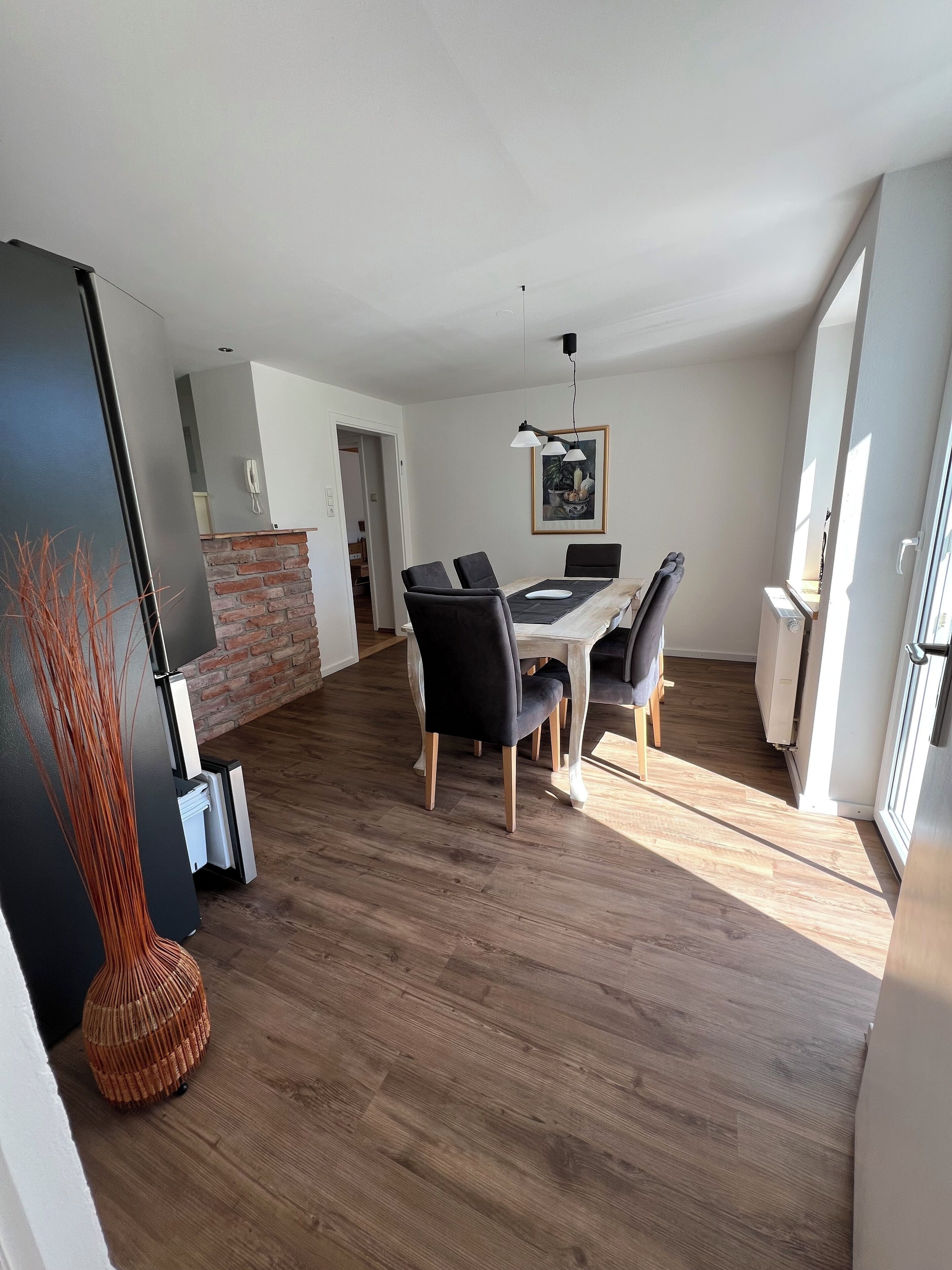A modern dining area with a wooden table and black chairs, a brick accent wall, and a hanging pendant light.