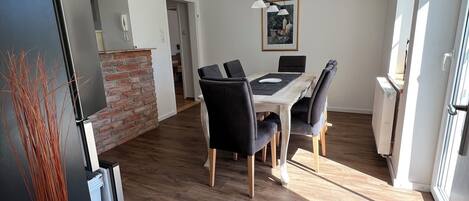 A modern dining area with a wooden table and black chairs, a brick accent wall, and a hanging pendant light.