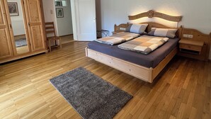 Un dormitorio con una cama de madera, una mesita de noche, un armario de madera y una alfombra gris sobre un suelo de madera.