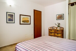 A bedroom with a bed, a wooden door, a dresser, and two framed pictures on the wall.