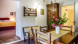 Una habitación con una cama, una mesa de comedor con sillas, un armario y un jarrón con flores.