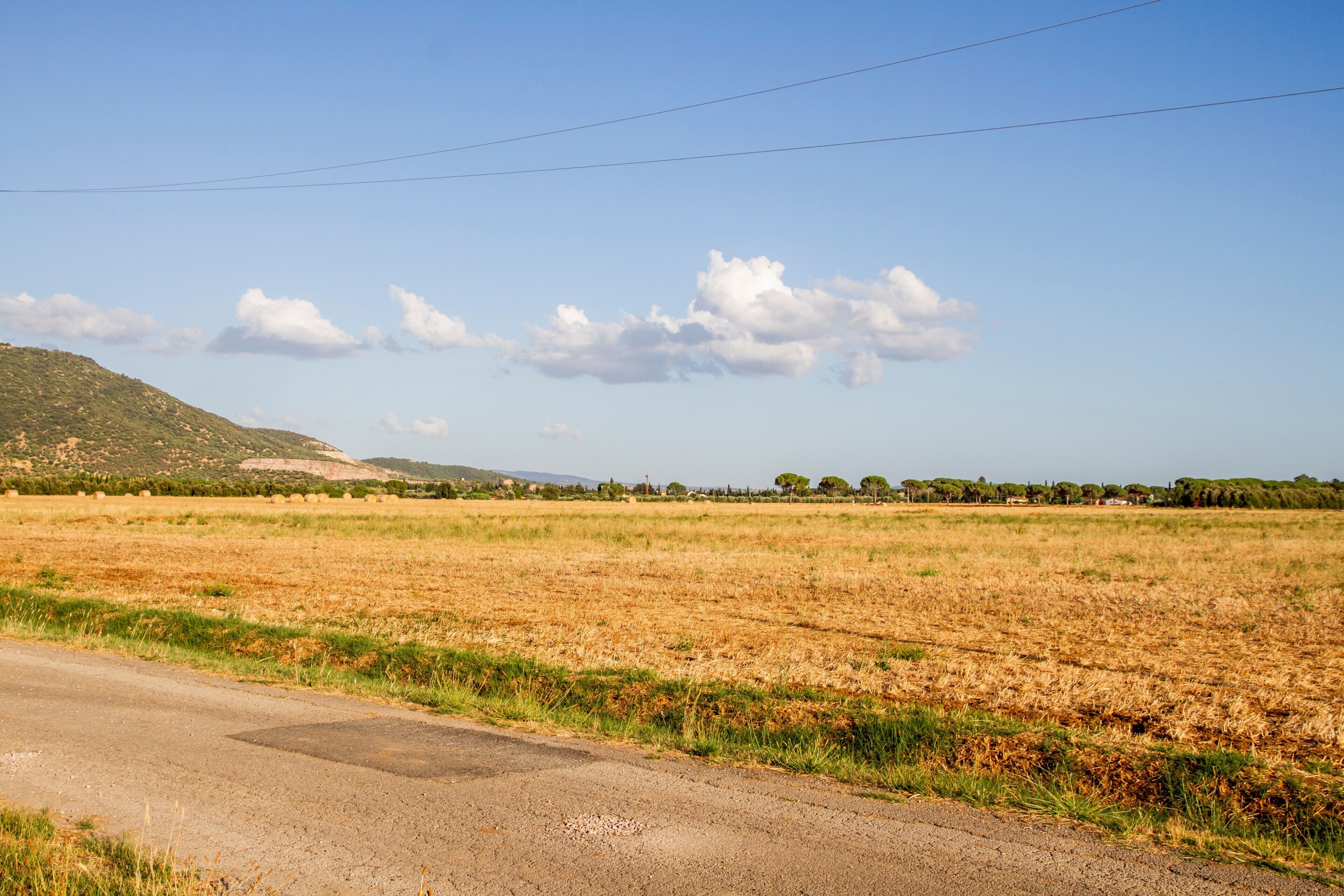 A rural landscape with a road, fields, and a hill in the background.