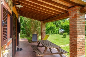 A covered patio with a wooden table and chairs, a brick pillar, and a view of a green garden. - Apartment 'Portico' with Private Terrace, Wi-Fi and Air Conditioning (Bagno Roselle)