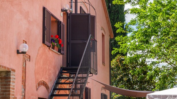 Un bâtiment avec un escalier, un balcon orné de fleurs et un arbre en arrière-plan.