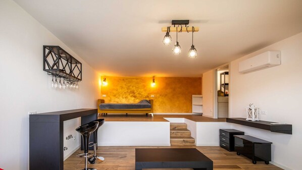 Een moderne woonkamer met een bank, een salontafel en een bar met barkrukken. Er is een trap die naar een ander niveau leidt.