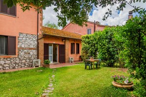 A house with a stone facade, a tiled roof, a small garden with a table and chairs, and a potted plant.